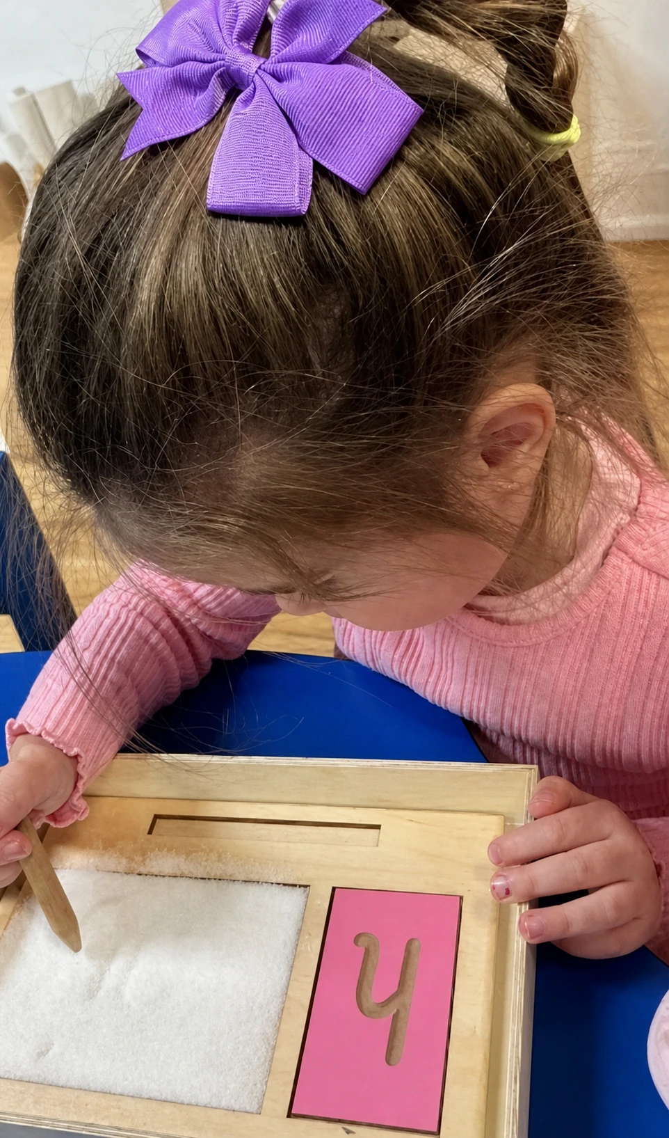 A preschool child tracing a tactile letter with a wooden stylus.